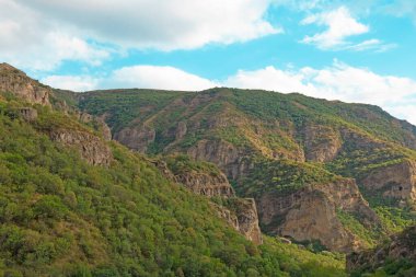 Güneşli ve bulutlu bir günde, gün batımında, altın saat boyunca Geghard manastırı yakınlarındaki Rocky ve orman dağları.