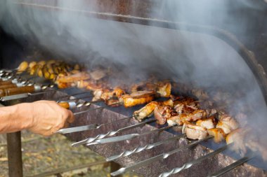 Brezilya usulü ızgarada nefis barbekü pişirme görüntüsü. Lezzetli domuz eti ve patates ızgarada kızartılıyor. Adamın eli bir şiş sapı tutuyor. Barbeküyü hazırlarken duman çıkıyor..