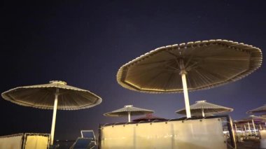 Güverte sandalyeleri plaj şemsiyeleri altında gece gökyüzü ve Samanyolu 'nun arka planına karşı, zaman aşımı