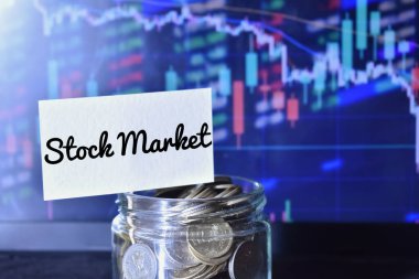 Arka planda bir mum ve çubuk grafiğine karşı borsada etiketli bozuk para çanağının yakın plan fotoğrafı..