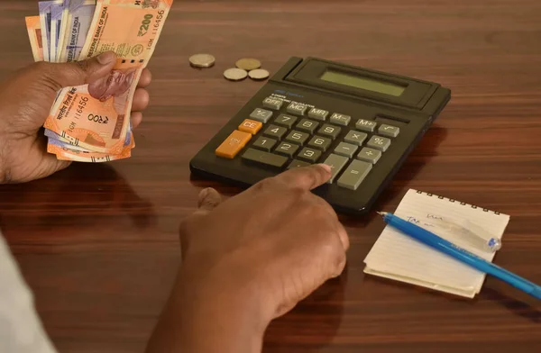 Bir adamın Hint banknotlarını tutarken ve ayın bütçesini hesaplarken çekilmiş yakın plan fotoğrafı..