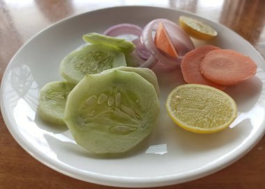 Restoranda beyaz bir tabağa salatalık, havuç ve soğan konmuş sebze salatasının yakın plan seçmeli resmi.