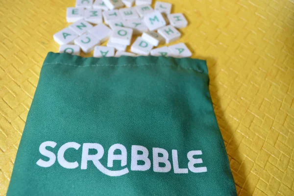A scrabble letter pouch laying with various letters spilled out of the pouch. Scrabble is a indoor game played.