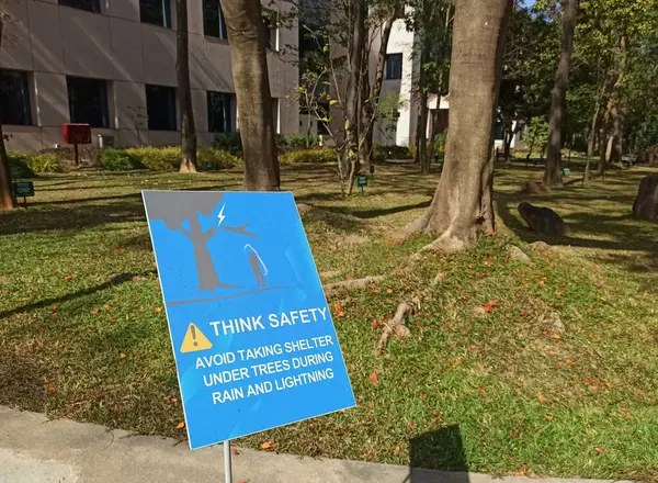 A closeup picture of safety measure board displayed to avoid Standing below tree during rain