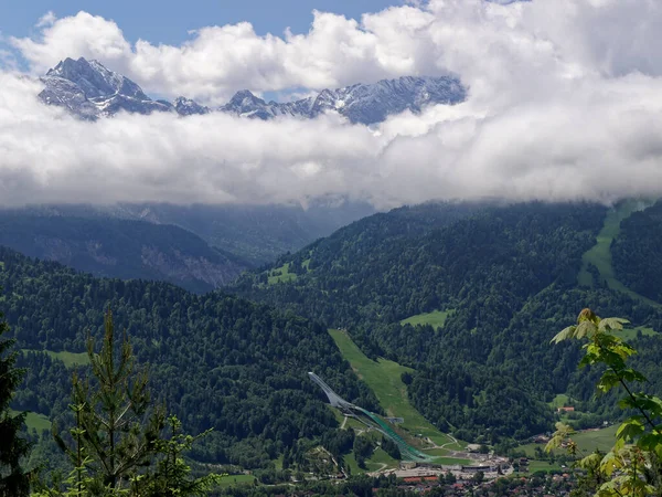 Wetterstein Dağları 'nın güzel manzarası, Garmisch-Partenkirchen kayak atlayışı ön planda. Bulutların arasındaki dağlar.