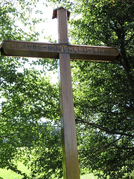Large wooden cross with the inscription Faith Hope Love on a hiking trail in the forest.