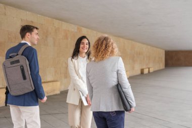 Modern bir binanın koridorunda yürüyen ve konuşan üç iş adamı iş meselelerini tartışıyor.