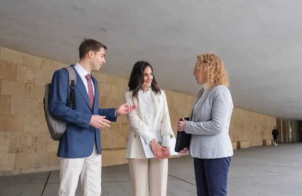 Modern bir binanın koridorunda yürüyen ve konuşan üç iş adamı iş meselelerini tartışıyor.