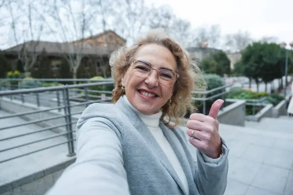 Takım elbiseli neşeli, kıdemli bir kadın dışarıda, kendine güvenini ve pozitifliğini gösteriyor.