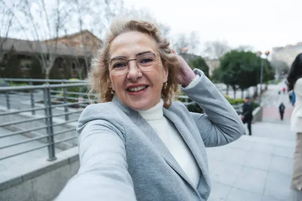 Gülümseyen son sınıf öğrencisi bir kadın şehrin sokaklarında selfie çekiyor, keyifli bir anın tadını çıkarıyor.