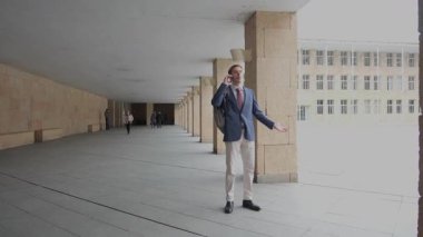 Genç bir iş adamı koridorda yürüyor ve telefonda konuşuyor.