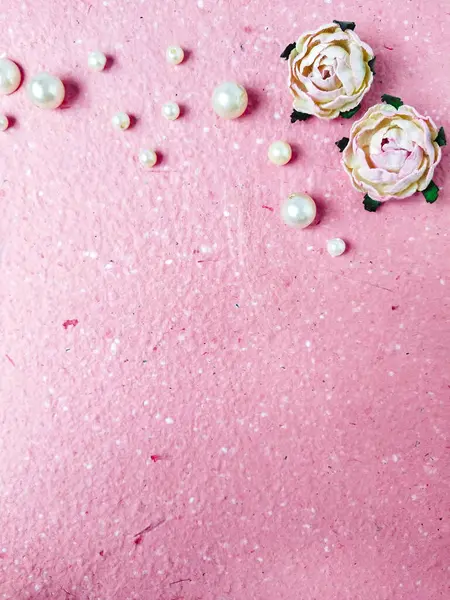 Pink paper background with pearls and roses. Flat lay, top view.