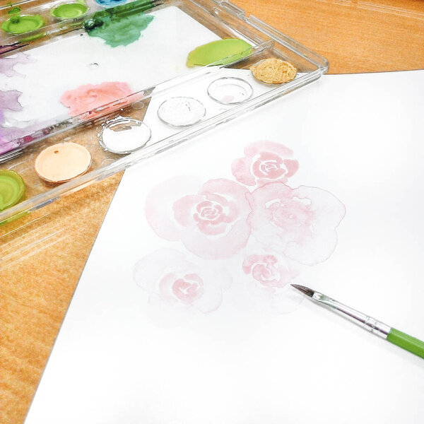 Watercolor paints and brushes on white paper with watercolor roses.