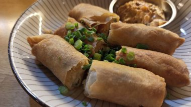 Fried spring rolls with green onions and sour cream on a plate