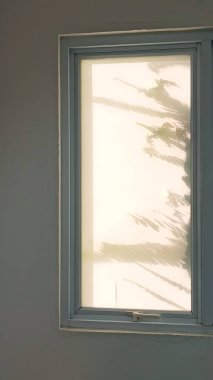Duvarında palmiye yaprağı gölgesi olan bir pencere, fotoğrafa yakın çekim. Duvarda gölgesi olan pencere