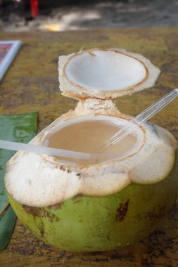 İçmeye hazır pipetli taze hindistan cevizi. Hindistan cevizi suyu musluktan hindistan cevizine dökülür. Hindistan cevizi sütü ve ahşap masa.