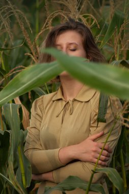 Young woman with long hair in yellow golden dress against the background of corn field in summer. Beauty and fashion.
