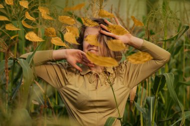Pozitif model kameraya gülümsüyor. Mısır tarlası ve manken mısır tarlasında yapraklar arasında. Sonbahar yaprakları dökülüyor