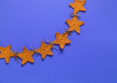 Mavi arka planda sarı örgü yıldız çelengi. El yapımı Noel süslemesi. Üst Manzara. Boşluğu kopyala.