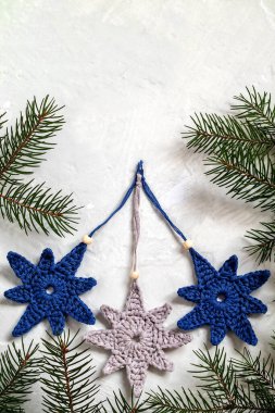 El yapımı örgü dekoru. Beyaz arka planda gri, mavi, tığ işi yıldız şekilli Noel ağacı oyuncakları ve köknar dalları. Boşluğu kopyala.