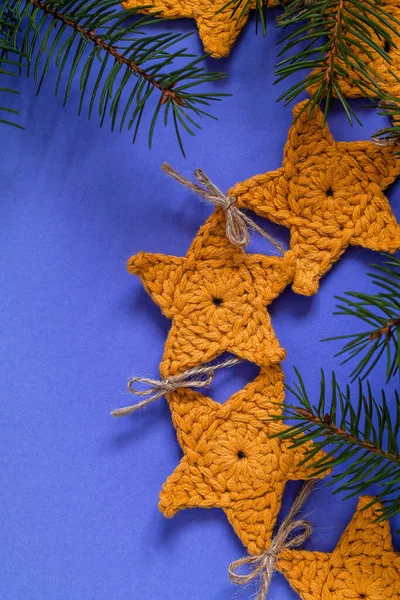 Christmas composition with yellow crochet star garland and fir tree branches on a blue background. Eco friendly Christmas decoration.