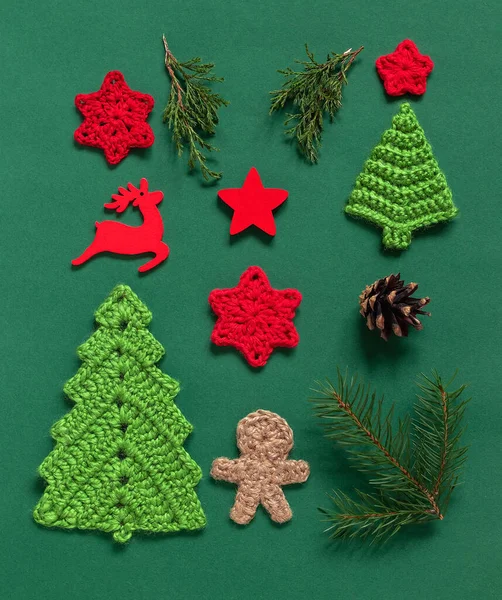 Christmas composition. Crochet Christmas tree, gingerbread man, snowflakes, wooden star and reindeer, cypres and fir tree branches on a green background. Flat lay. Top view.