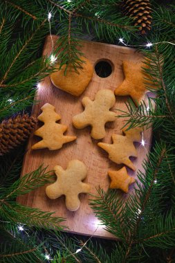 Köknar dalları ve bokeh lambaları arasında tahta bir tahtanın üzerinde taze ev yapımı zencefilli kurabiye. Noel pastanesi.