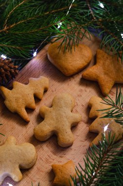 Köknar dalları ve bokeh ışıkları arasında tahta bir tahtanın üzerinde geleneksel Noel kurabiyeleri. Mutlu Noeller ve mutlu yıllar konsepti.