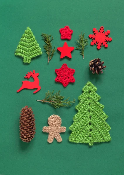 Christmas composition. Crochet Christmas tree, gingerbread man, snowflakes, wooden star and reindeer, cypres branches on a green background. Flat lay. Top view.