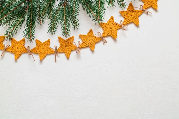 Yellow crochet garland on a white background. Christmas handmade star shaped garland and fir tree branches. Christmas decoration. Copy space.