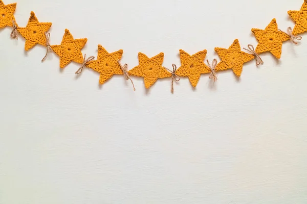 stock image A long yellow crochet garland hanging against a white wall. Christmas handmade star shaped garland. Christmas decoration. Copy space.