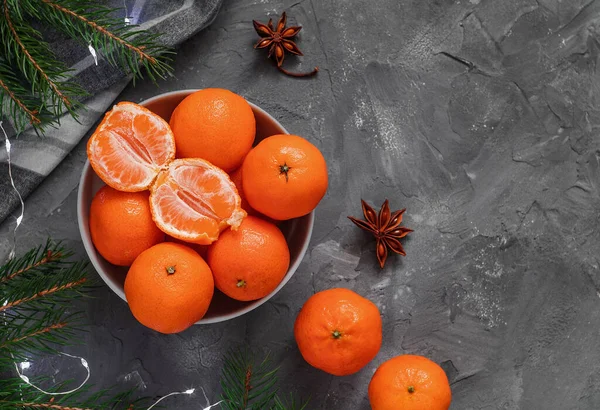 stock image Mandarine oranges in a bowl among fir tree branches, star anise on a gray background. Copy space.