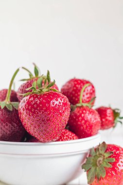 Beyaz arka planda kırmızı çilekli beyaz bir kase..