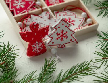 Beyaz arka plandaki bir kutuda kırmızı ve beyaz Noel oyuncakları. Tahta Noel ağacı ve Noel Meleği. Noel süslemesi.