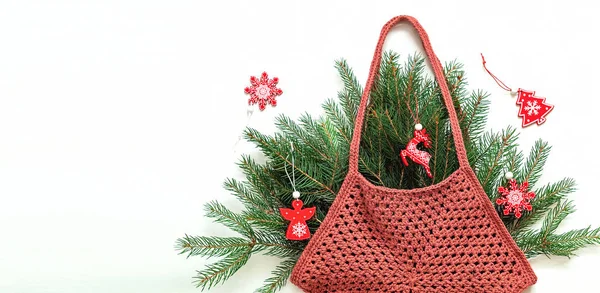 白い背景にモミの木の枝やクリスマスの木製のおもちゃで形成されたブルゴーニュかぎ針編みの袋の六角形 手作りショッピングメッシュバッグ スペースのコピー — ストック写真