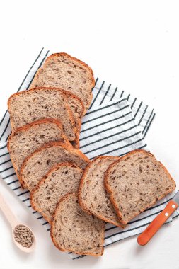 Beyaz arka planda keten bir peçeteye dilimlenmiş tahıllı ekmek ve keten keten. Sağlıklı fırın ürünü.