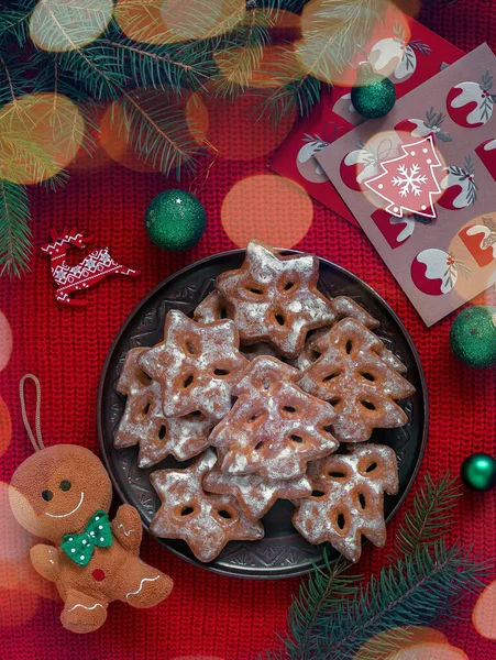 Plate with gingerbread glazed cookies and Christmas decor on a red knitted background with garland lights.