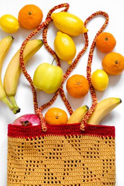 Taze meyve (muz, limon, elma, mandalina, nar) sarı bir tığ işi çantada. Çevre dostu alışveriş için el yapımı pamuk torbası. Sıfır atık.