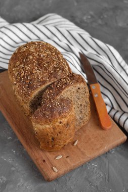 Ahşap bir tahtada dilimlenmiş çavdar ekmeği ve gri bir arka planda çizgili kumaş..