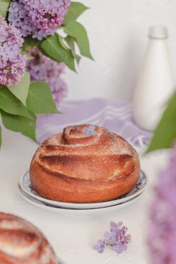 Süt şişesi ve leylak çiçekli taze tarçınlı çörekler. Kanelbullar - İsveç tarçını ruloları.