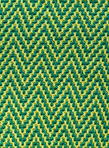 Knitted texture with chevron pattern. Texture of mosaic fabric with yellow green geometric ethnic pattern. Crochet mosaic pattern.