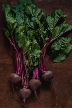 Koyu ahşap arka planda yeşil yapraklı taze organik pancar kökleri..