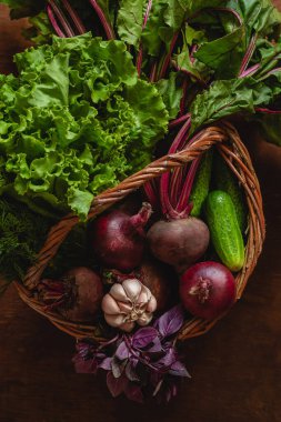 Tahta bir arka planda hasır sepette çeşitli sebzeler. Taze marul, pancar kökü, fesleğen, sarımsak, salatalık. Sağlıklı vejetaryen yemekleri.