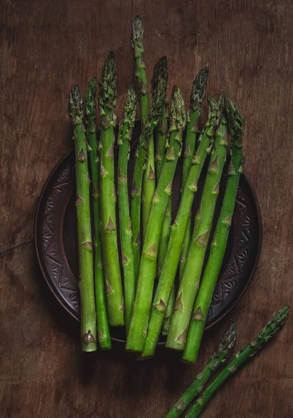 Green asparagus on a dark round clay plate on a wooden background. Top view.
