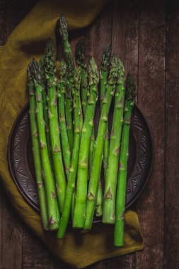 Koyu seramik tabakta yeşil kuşkonmaz ve ahşap arka planda keten peçete. Üst görünüm.