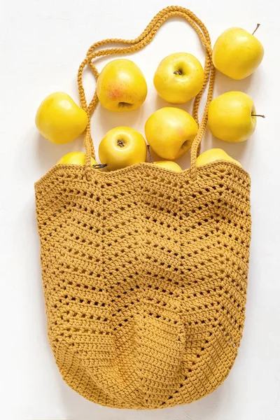 Eco crochet net bag with fresh organic golden apples on a white background.