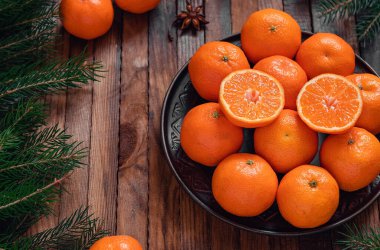 Kahverengi bir tabakta taze mandalinalar ve koyu bir tahta üzerinde köknar dalları olan Noel kompozisyonu..