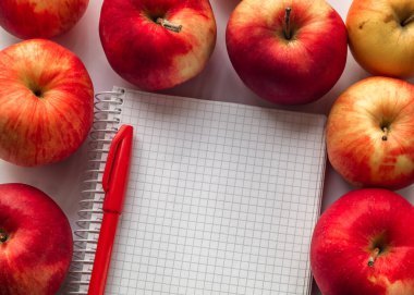 Beyaz defter, kırmızı kalem ve kırmızı elmaları aç. Boşluğu kopyala.