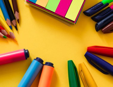 Sarı arka planda parlak renkli okul malzemeleri..
