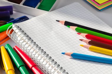 Okul malzemeleri arasında açık bir defterin üzerinde renkli kalemler var. Okul konseptine dönelim..